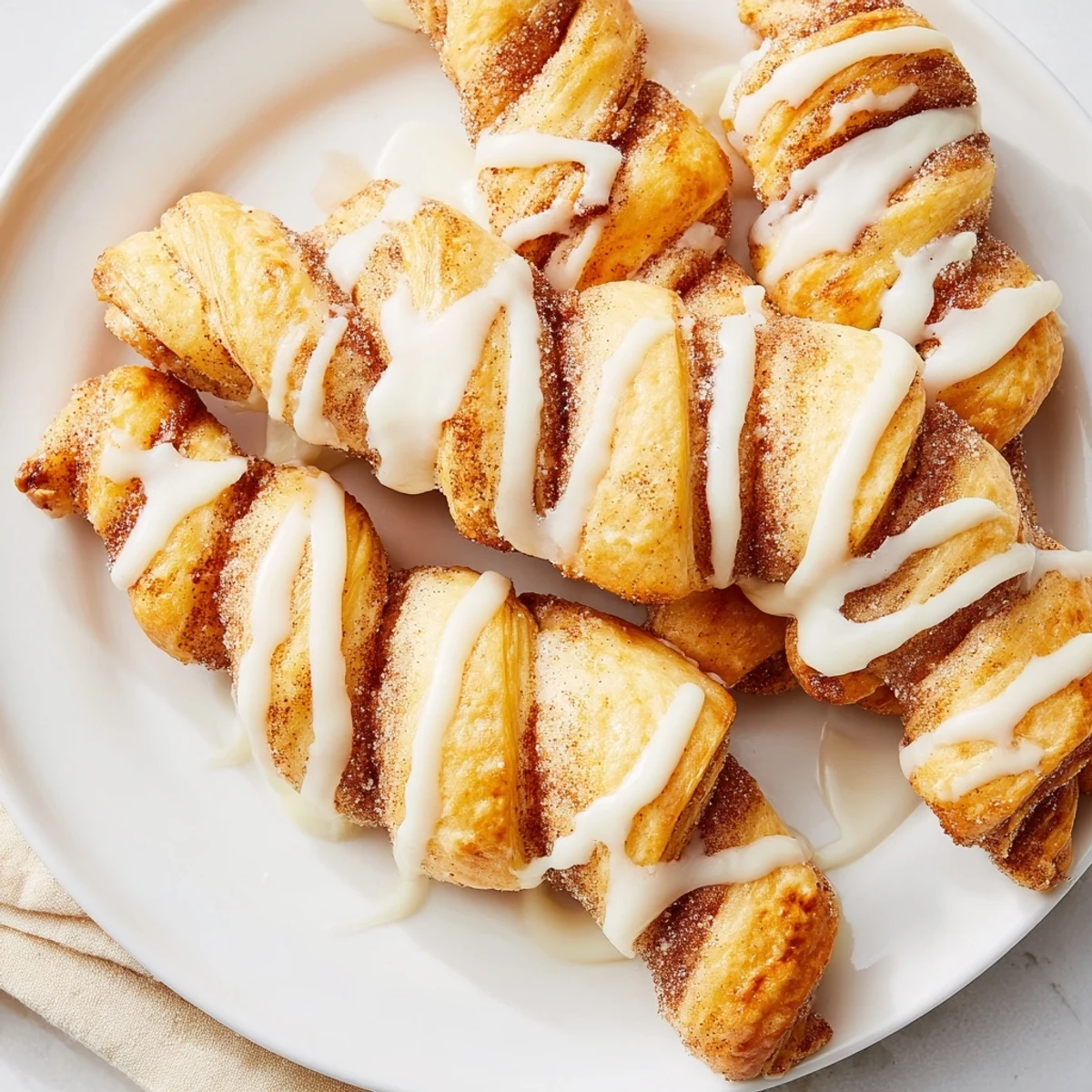 Flaky air-fryer cinnamon roll twists, warm and golden, are drizzled with sweet vanilla glaze for a perfect treat.