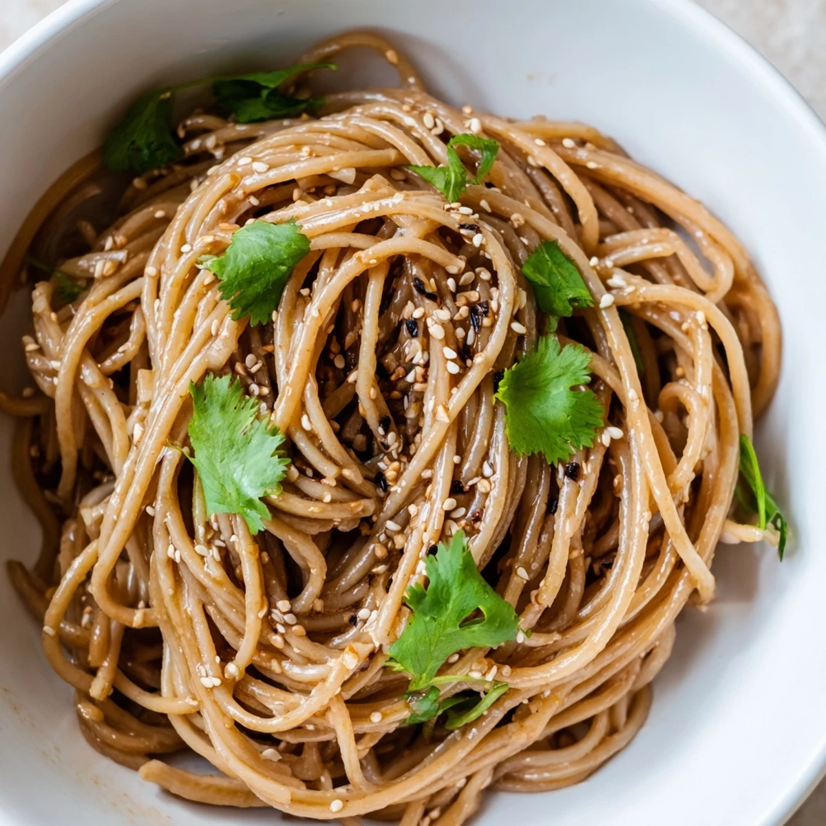 A close-up of Spicy Sesame Noodle Salad topped with toasted sesame seeds, peanuts, and vibrant cilantro.