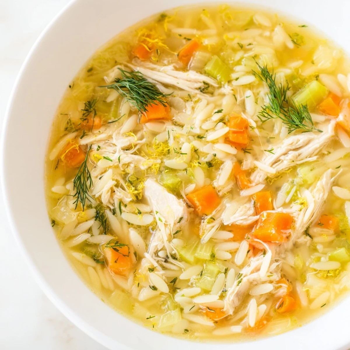 Bright and comforting Chicken Lemon Orzo Soup steaming in a rustic bowl, garnished with fresh dill and lemon slices.