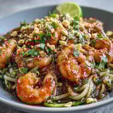 Colorful Asian Noodle Bowl featuring sautéed shrimp, crunchy veggies, and a drizzle of savory lime sauce.