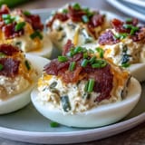 Cream cheese and jalapeño deviled eggs garnished with crispy bacon bits, perfect for spicy appetizer lovers.  