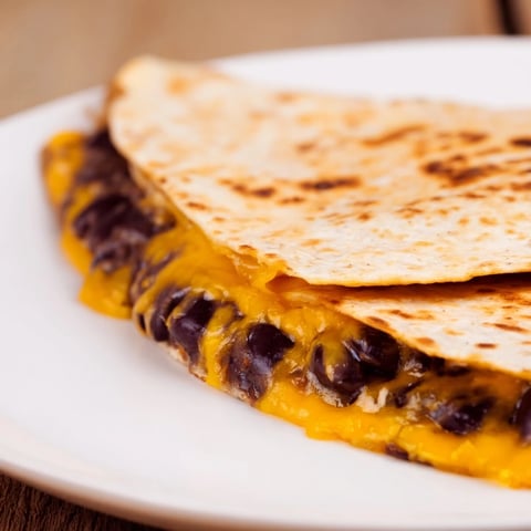 Golden, melty Bean & Cheese Quesadillas are sizzling in a pan, ready to be flipped for a yummy meal.