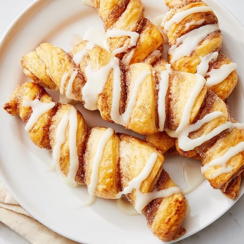 Flaky air-fryer cinnamon roll twists, warm and golden, are drizzled with sweet vanilla glaze for a perfect treat.