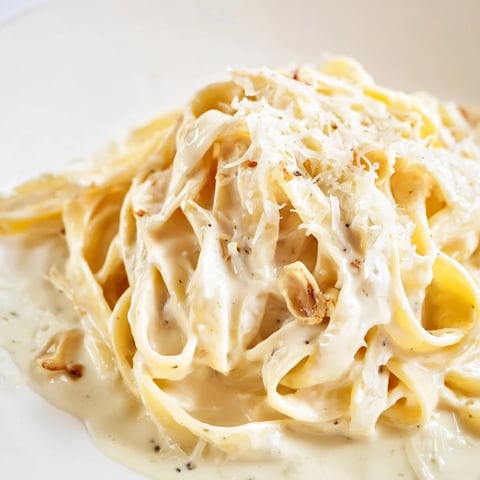 Steaming Roasted Garlic Cream Pasta twirls on a fork beside a wedge of golden Parmesan and fresh parsley.  