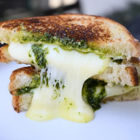 A close-up of golden, crispy Spinach Pesto Grilled Cheese sandwich slices, revealing gooey melted cheese and vibrant green pesto on sourdough bread.