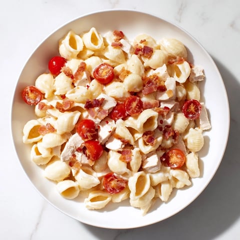 A close-up of BLT Chicken Pasta Salad in a white bowl, featuring grilled chicken chunks, crisp romaine, and halved cherry tomatoes.  