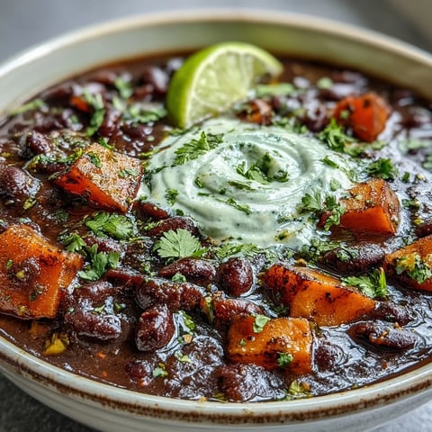 Smoky black bean and sweet potato soup with lime crema in a rustic bowl, garnished with fresh cilantro and a lime wedge.