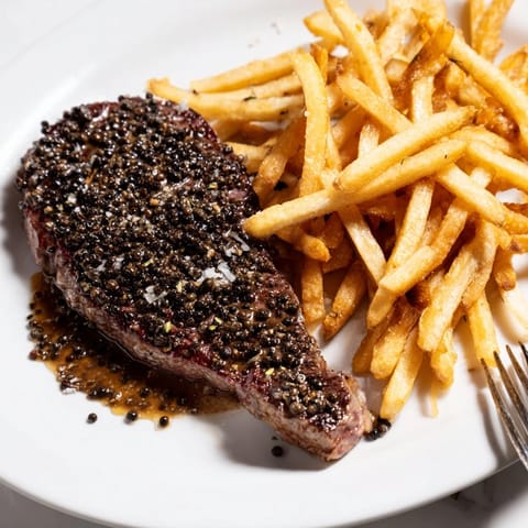 Sizzling classic peppercorn ribeye steak served with golden, crunchy fries for a feast.  