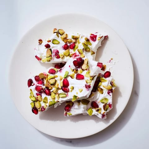 Vibrant pink Frozen Yogurt Bark topped with juicy pomegranate and pistachios, ready to enjoy.
