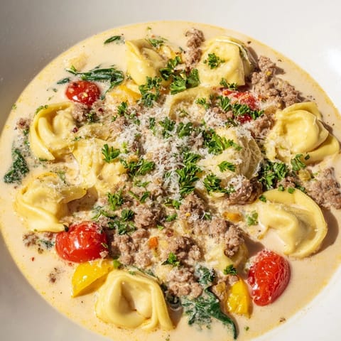 A steaming bowl of comforting Tortellini Beef Soup with fresh basil, Parmesan, and juicy cherry tomatoes.