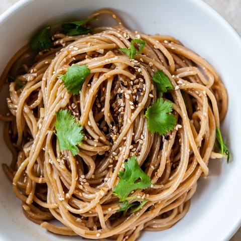 A close-up of Spicy Sesame Noodle Salad topped with toasted sesame seeds, peanuts, and vibrant cilantro.
