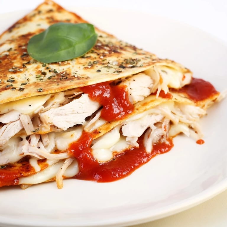 Close-up of a flavorful tortilla pizza wrap with chicken, showing layers of sauce, cheese, and chicken.