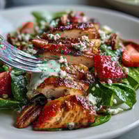 Juicy grilled chicken slices rest on fresh spinach and sliced strawberries, topped with creamy poppy seed dressing for a light summer meal.