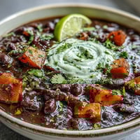 Smoky black bean and sweet potato soup with lime crema in a rustic bowl, garnished with fresh cilantro and a lime wedge.